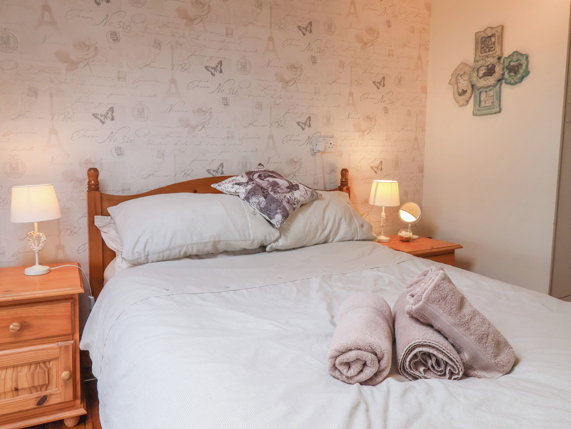 Una cama bien tendida con almohadas, una lámpara de noche, una mesita de madera y una pared decorada.