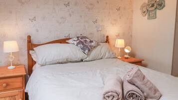 Una cama bien tendida con almohadas, una lámpara de noche, una mesita de madera y una pared decorada.
