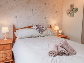 Una cama bien tendida con almohadas, una lámpara de noche, una mesita de madera y una pared decorada.