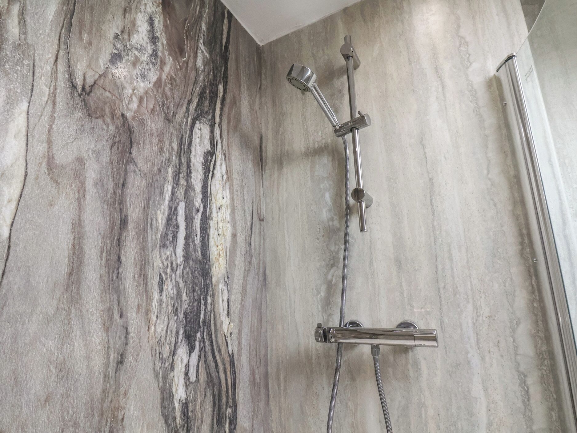A modern shower with a marble wall backdrop.