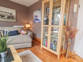 Una sala de estar con un sofá, un aparador de vidrio con libros, una lámpara y una planta.