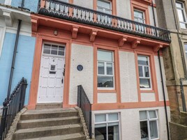 Un edificio de varios pisos con una puerta blanca, varias ventanas y un balcón con barandillas negras.