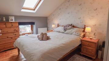 Un dormitorio con tragaluz, cómoda de madera, cama con toallas y pared estampada.