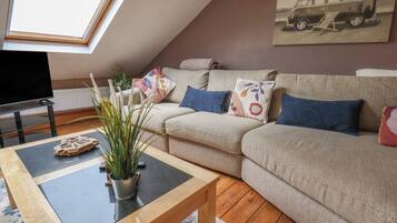 A cozy living room with a sofa, a coffee table, a TV, and a skylight.
