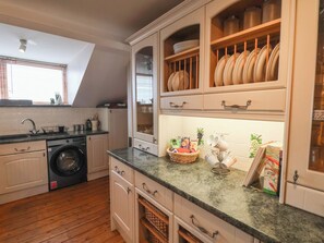 Une cuisine équipée d’un lave-linge, d’un évier et de placards contenant de la vaisselle.
