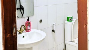Ein Badezimmer mit weißen Fliesen, einem Waschbecken, einem Spiegel, einer Dusche und einer Toilette.