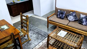 Ein Zimmer mit einem Holzhocker, einer Couch mit gemusterten Kissen, einem kleinen Tisch mit kariertem Deckblatt und einem Teppich mit Muster.