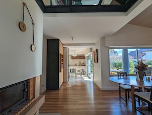 Ein modernes Interieur mit Kamin, Holzboden, einer Essecke mit rundem Tisch und einer Küche im Hintergrund.