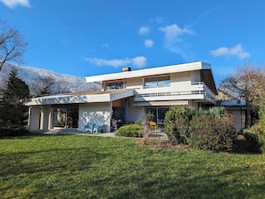 Une maison moderne à deux étages, dotée d’un toit plat, de grandes fenêtres et d’un balcon.
