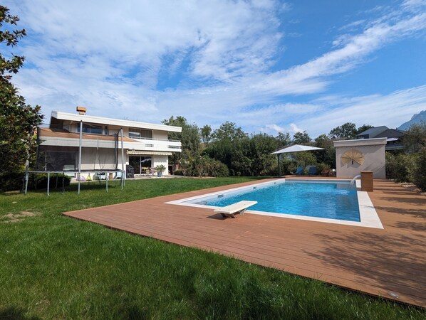 Une maison moderne à deux étages, dotée d’une piscine, d’un patio et d’un espace extérieur aménagé et couvert.