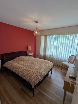 Une chambre à coucher avec un lit, un bureau, une chaise, une lampe et une fenêtre avec des rideaux.