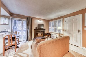 A living room with a sofa, a television, a fireplace, and a dining area with chairs and a table. - North Base Studio with Pool, Hot Tub, Tennis! (The Blue Mountains)