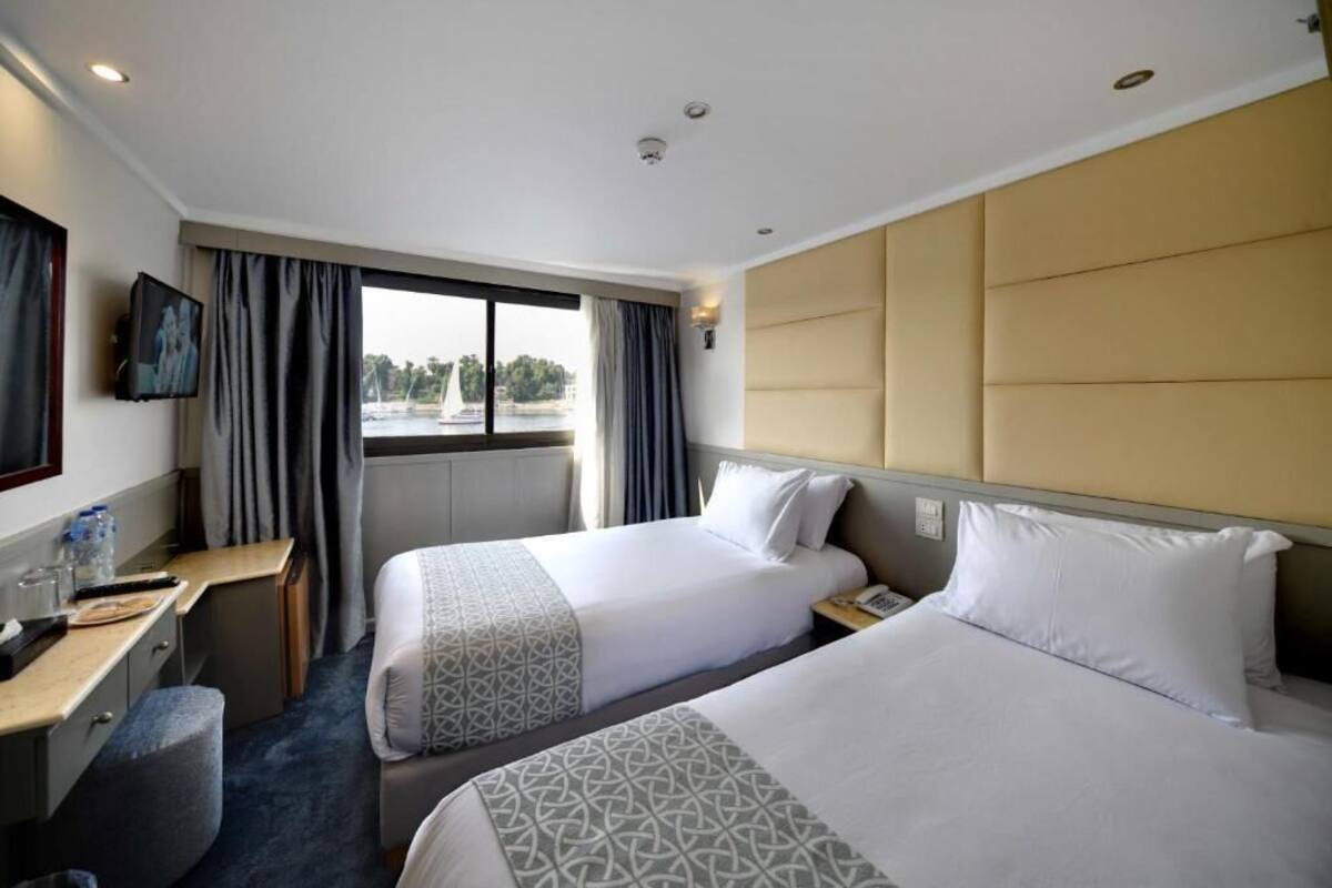 A hotel room with two beds, a desk, a chair, a TV, and a window with curtains.
