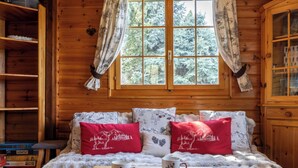 Ein gemütliches Cabin-Zimmer mit Holzvertäfelung, einem großen Fenster mit Vorhängen, einem Bett mit gemusterten Kissen und einem Tisch mit zwei Tassen und Untertassen.