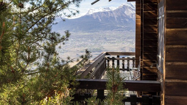 Eine Holzhütte mit einem Balkon mit Blick auf eine gebirgige Landschaft.