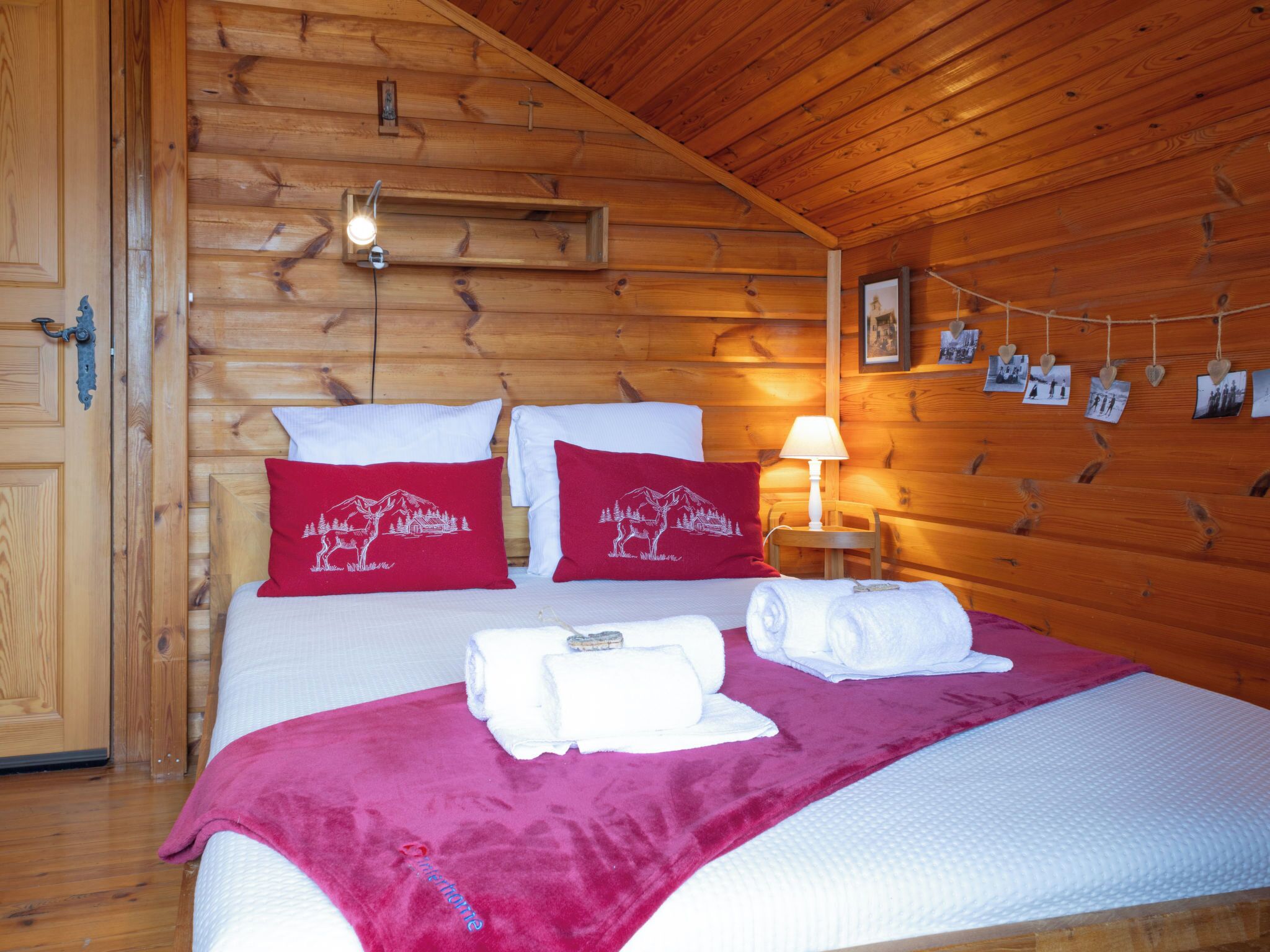 Une chambre dans une cabane en bois, avec un lit, des oreillers, une lampe et un mur décoré de photos.