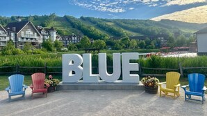 Un letrero con la palabra 'BLUE' en letras grandes, rodeado de sillas Adirondack en azul, rojo y amarillo.