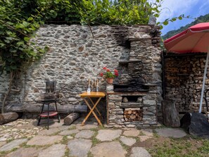 Eine Steinsäule mit einem kleinen Tisch und Stühlen, einem Grill und einem Holzstoß.