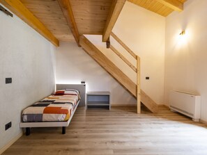 Un dormitorio con techo de madera, una litera, una mesita pequeña y un radiador.