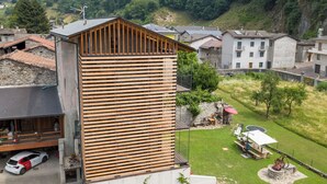 Een modern gebouw met een houten gevel, een balkon en een verzorgd gazon met terrasmeubels.