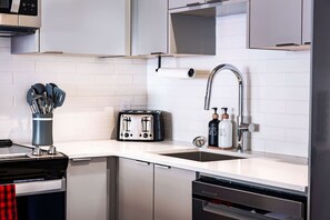 Eine moderne Küche mit einer Edelstahl-Dunstesse, einem Toaster, einer Spüle mit Armatur und einem Geschirrgestell.