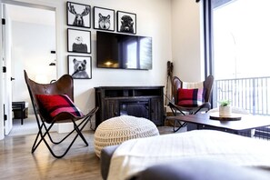 Ein modernes Wohnzimmer mit Kamin, zwei Ledersesseln, einem runden Ottomanen und einem an der Wand befestigten Flachbildfernseher.