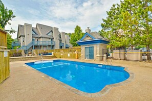 Une piscine bordée de pierres, une terrasse en bois et, au fond, un bâtiment avec un toit bleu.