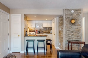 A kitchen with white cabinets, a microwave, and a stone accent wall. There are two stools and a small table. - Mountainside at North Base: Pool, Hot Tub, Tennis! (The Blue Mountains)