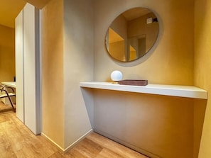 Ein Zimmer mit einem runden Spiegel an der Wand, einem weißen Regal und einem kleinen Tisch mit einem Stuhl.