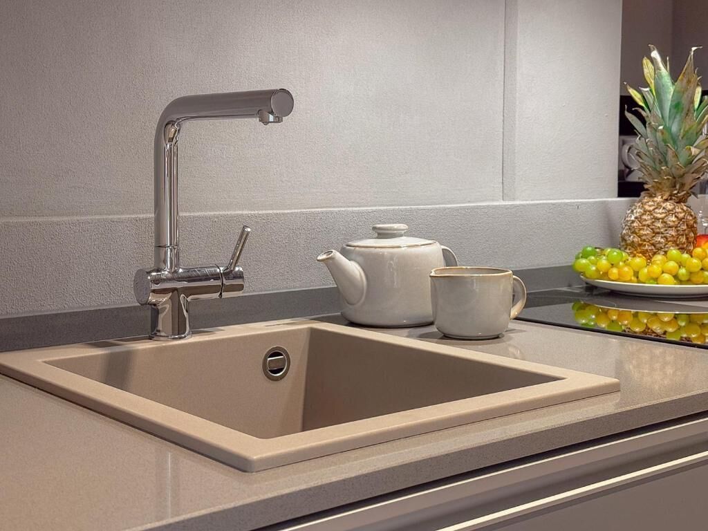Una cocina moderna con un lavamanos de acero inoxidable, un hervidor blanco y una taza.