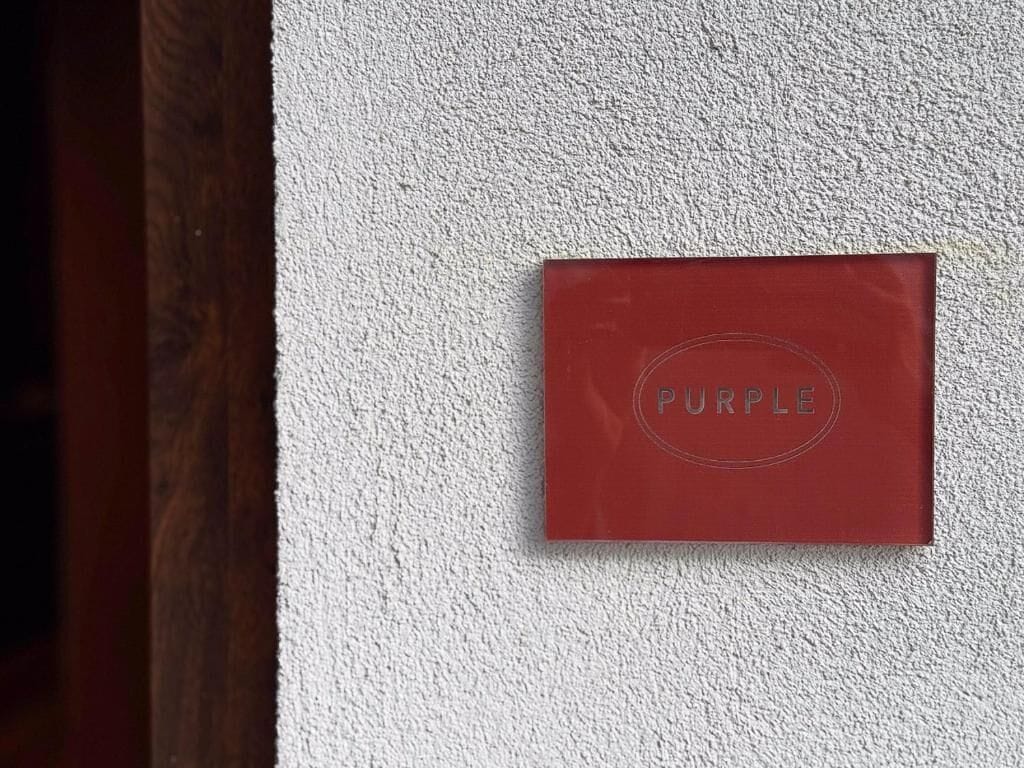 A red plaque with the word 'PURPLE' on a textured white wall.