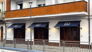 A building with a white facade, a balcony with a metal railing, and three awnings with a logo. - Blu Rooms - Room to Rest (Civitanova Marche)