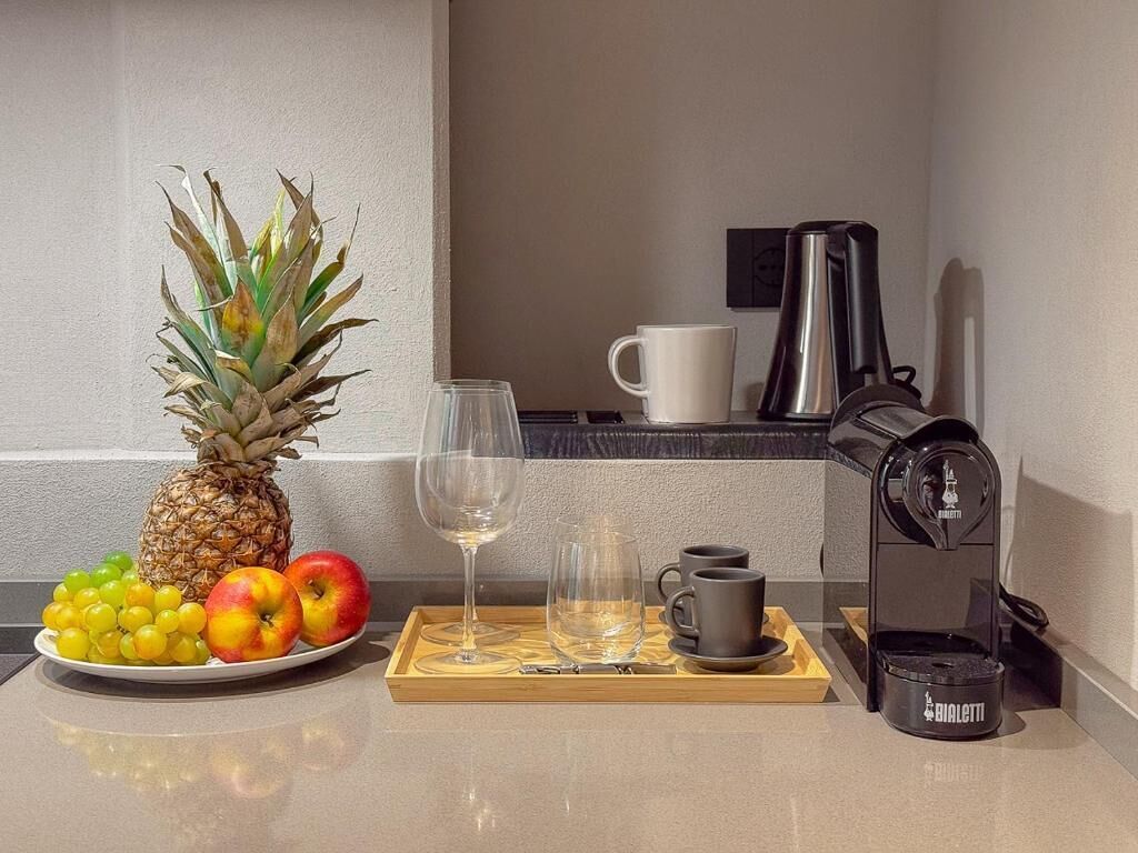 A kitchen counter with a pineapple, grapes, and apples, a coffee maker, a wine glass, and a coffee pot.