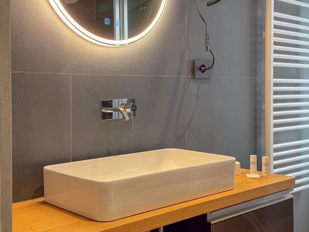 Un baño con un lavamanos rectangular, un espejo con luz circular y un perchero para toallas.