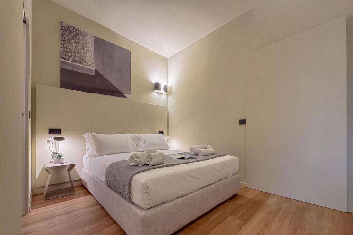 Een slaapkamer met een bed, nachtkastje, lamp en decoratie aan de muur.