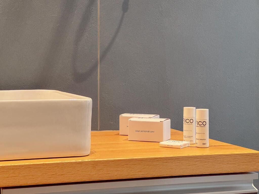 Una encimera de madera con un objeto rectangular blanco, tres cajas blancas con la etiqueta 'your personal care' y dos botellas blancas con la marca 'FICO'.