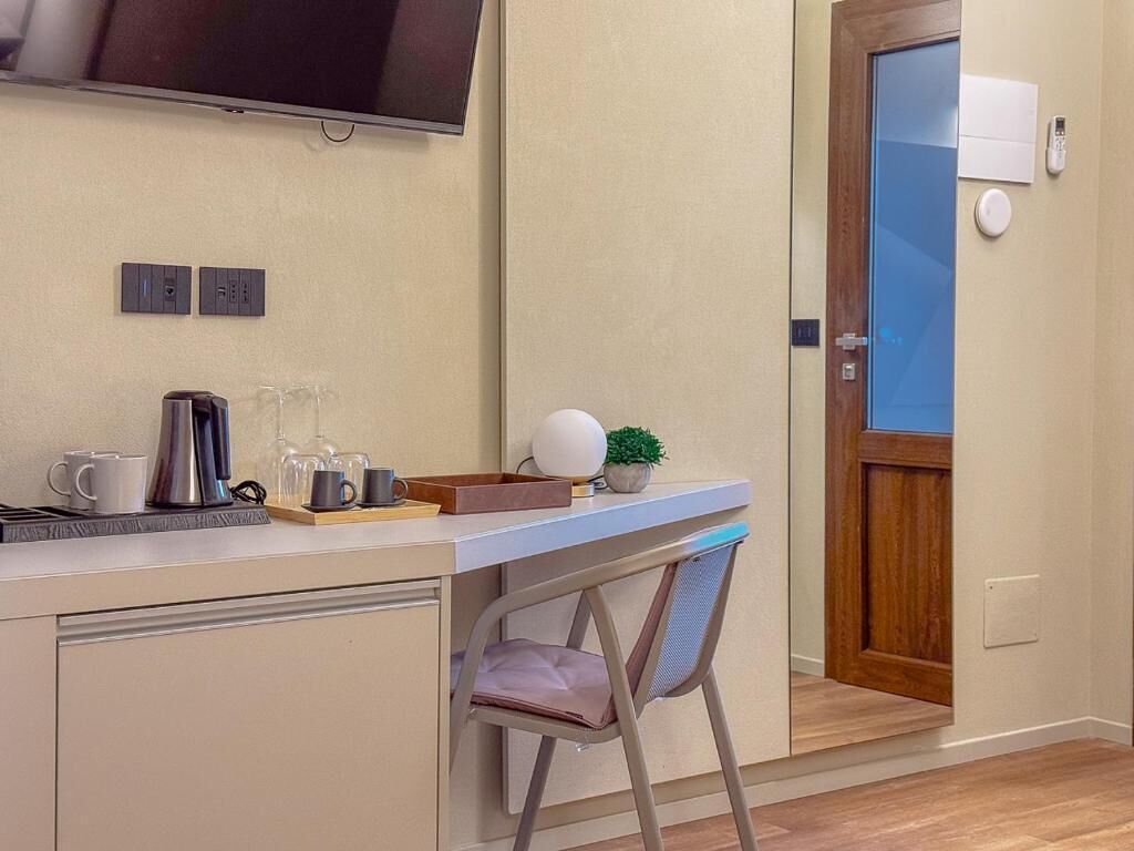 Ein kleines Zimmer mit Schreibtisch, Stuhl, Fernseher und einer Tür mit Glasfenster.