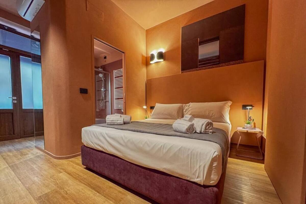 Een moderne hotelkamer met een groot bed, een nachtkastje, een wandlamp en een deur naar een douchecel.