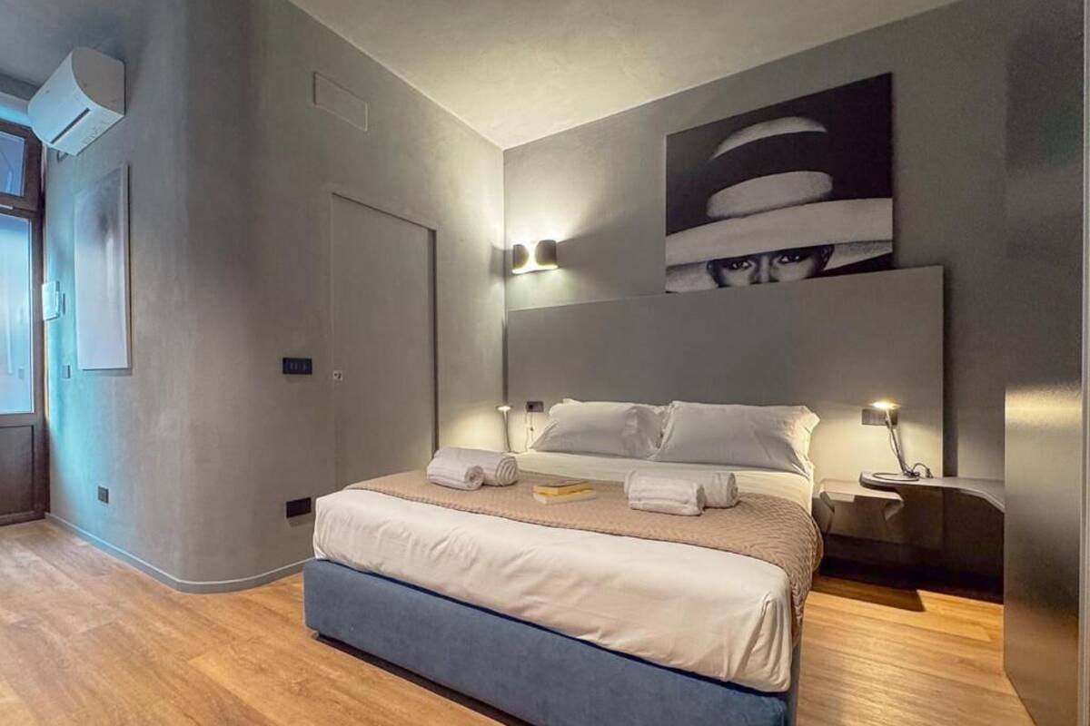 Een moderne slaapkamer met een groot bed, nachtlampjes, een hoofdbord met een afbeelding en een houten vloer.