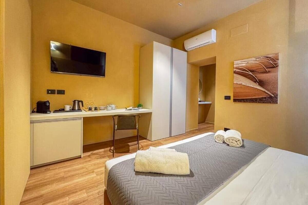 Een kleine hotelkamer met een bed, een bureau, een stoel, een televisie en een airconditioning.