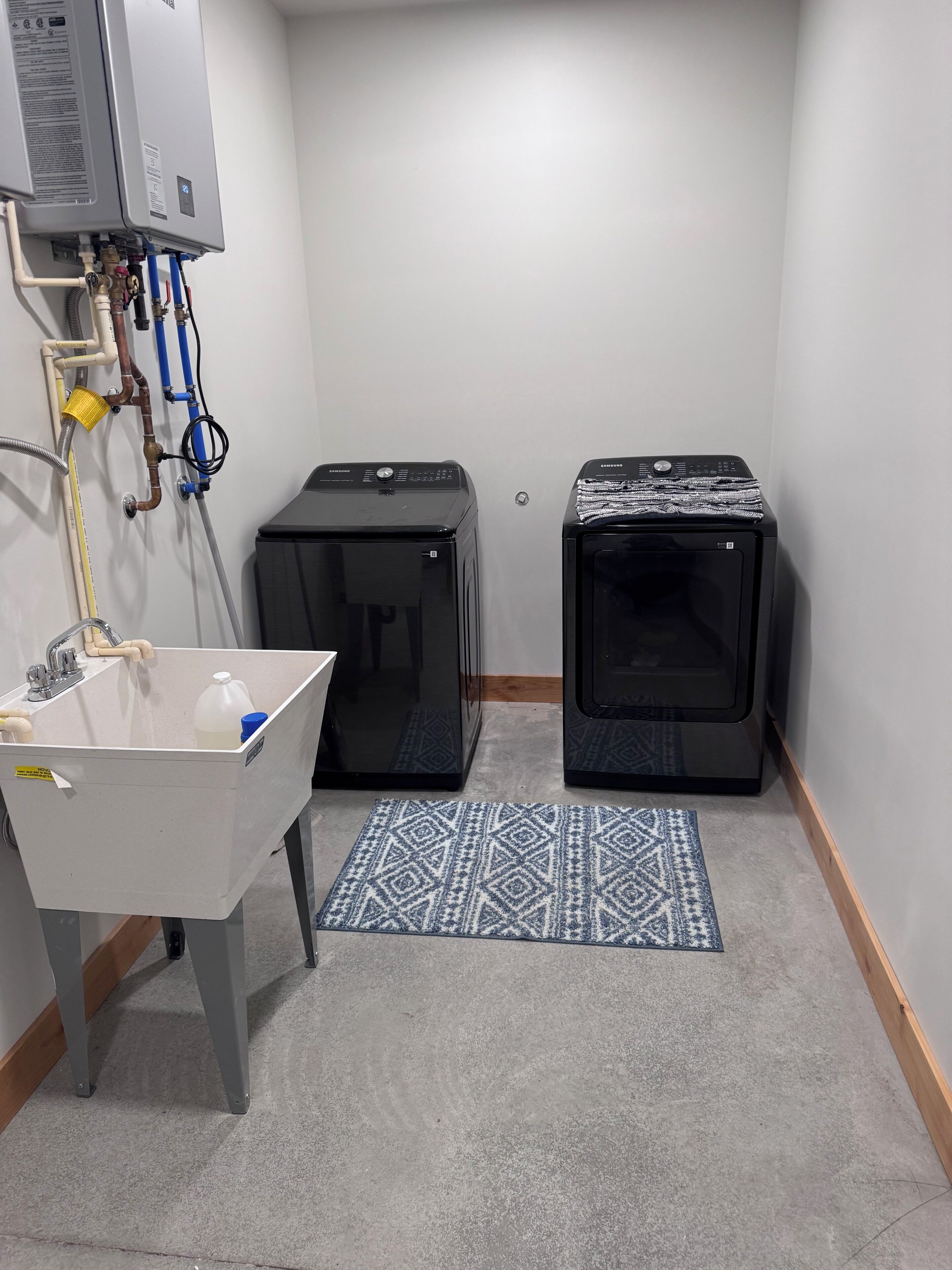 A small utility room with a sink, two black washing machines, and a water heater.