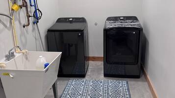 A small utility room with a sink, two black washing machines, and a water heater.