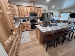 A kitchen with wooden cabinets, stainless steel appliances, a granite countertop, and a bar stool seating area.