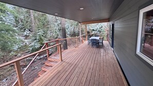 Una terraza de madera con una mesa y sillas, rodeada de un bosque.