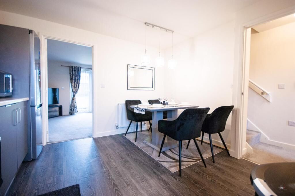 A modern kitchen with dark wooden flooring, a dining area with a table and chairs, and a visible staircase.