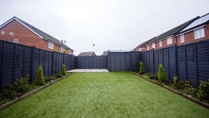 A residential backyard with a well-maintained lawn, a wooden fence, and houses in the background. - Spacious Luxurious Serviced Accommodation 2 (Coventry)
