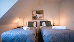 A room with two beds, each with a quilted blue bedspread and a rolled white towel. There is a painting on the wall above the beds. - Spacious Luxurious Serviced Accommodation 2 (Coventry)
