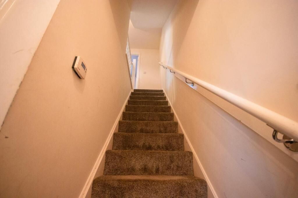 Eine Teppich-Treppe mit Handlauf, einem Rauchmelder und einer Tür am oberen Ende.