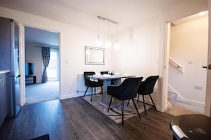 Una cocina moderna con suelo de madera oscura, una zona de comedor con mesa y sillas, y un pasillo que lleva a otra habitación.
