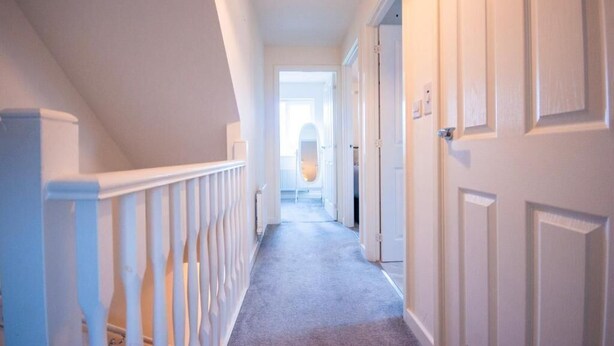 A hallway with white walls, a carpeted floor, and a white railing. - Spacious Luxurious Serviced Accommodation 2 (Coventry)